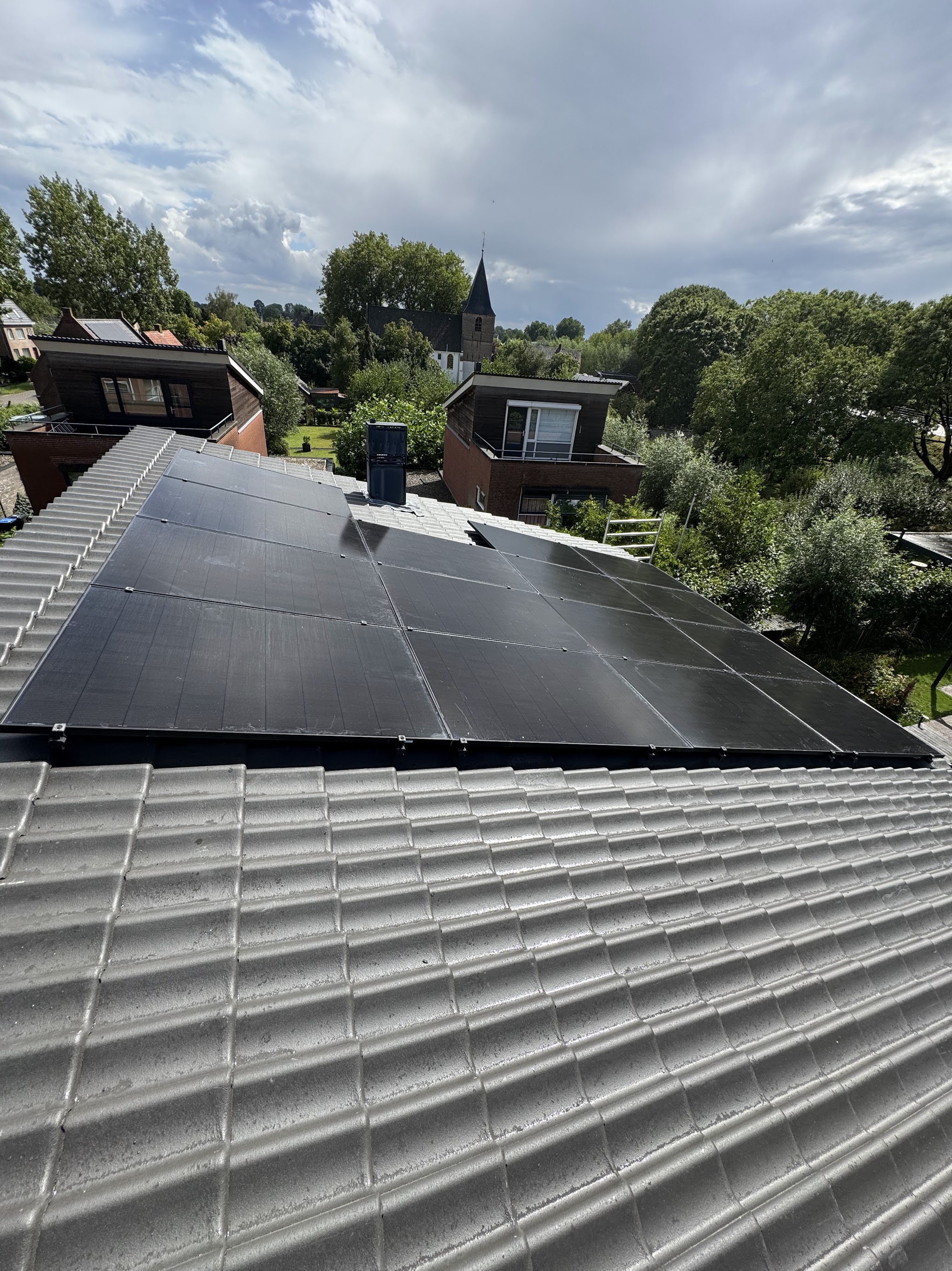 Dak met zwarte panelen, met uitzicht over bomen en een kerktoren