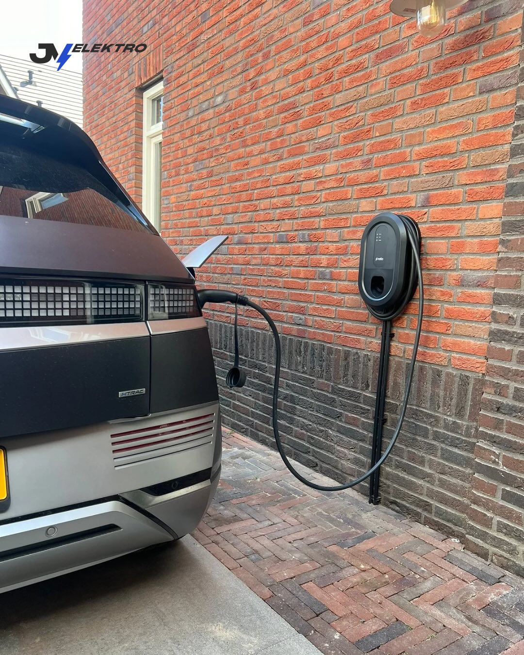 Laadpaal aan een bakstenen gevel met een elektrische auto aan de lader